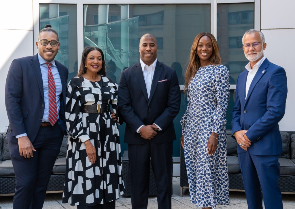 Three black men in suites and two black women in dresses pose in a conference room